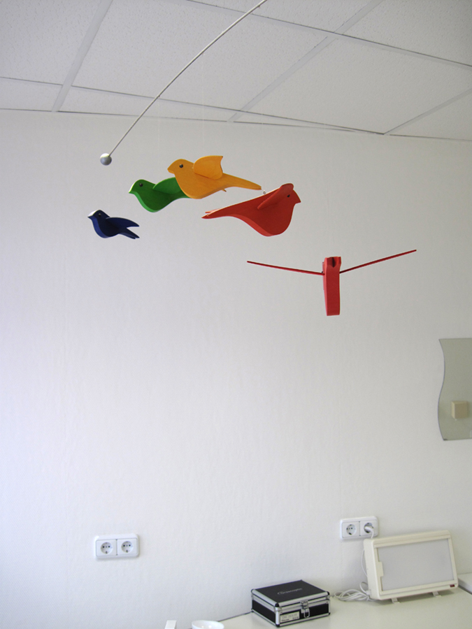 Detailfoto eines Deckenmobiles von bunten Holzvögeln.