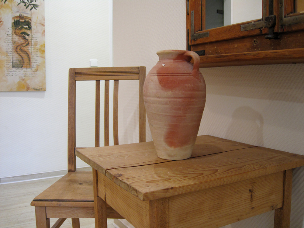 Detailaufnahme einer Tonvase, die als Dekoobjekt auf einem Holztisch steht.