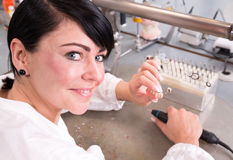 Eine Zahntechnikerin schleift Zahnprothesen.